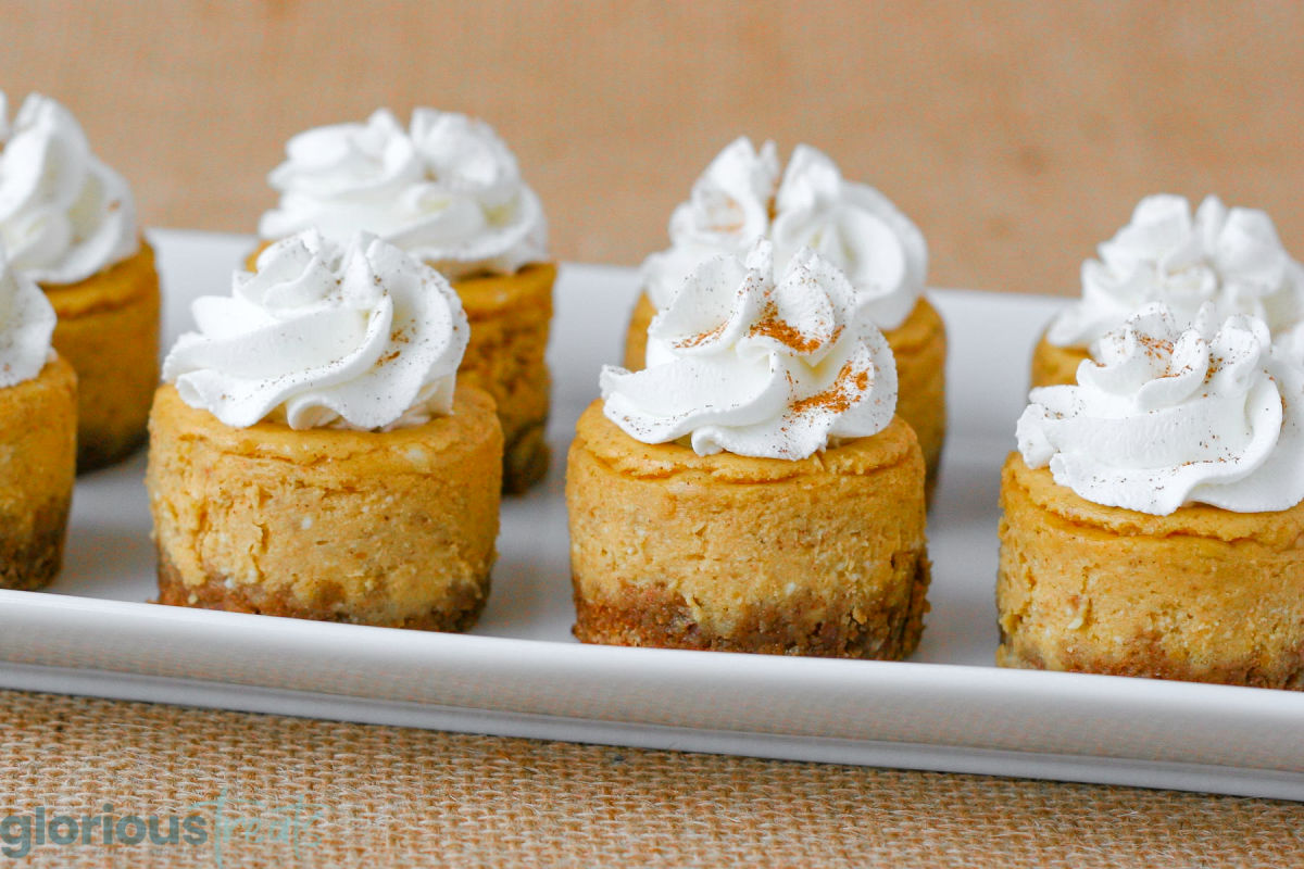 Eight mini pumpkin cheesecakes on a white rectangular platter.