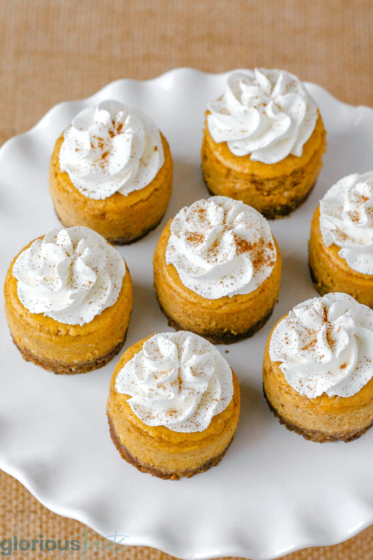 Top down angled view of white frilled cake stand with whipped cream topped mini pumpkin cheesecakes.