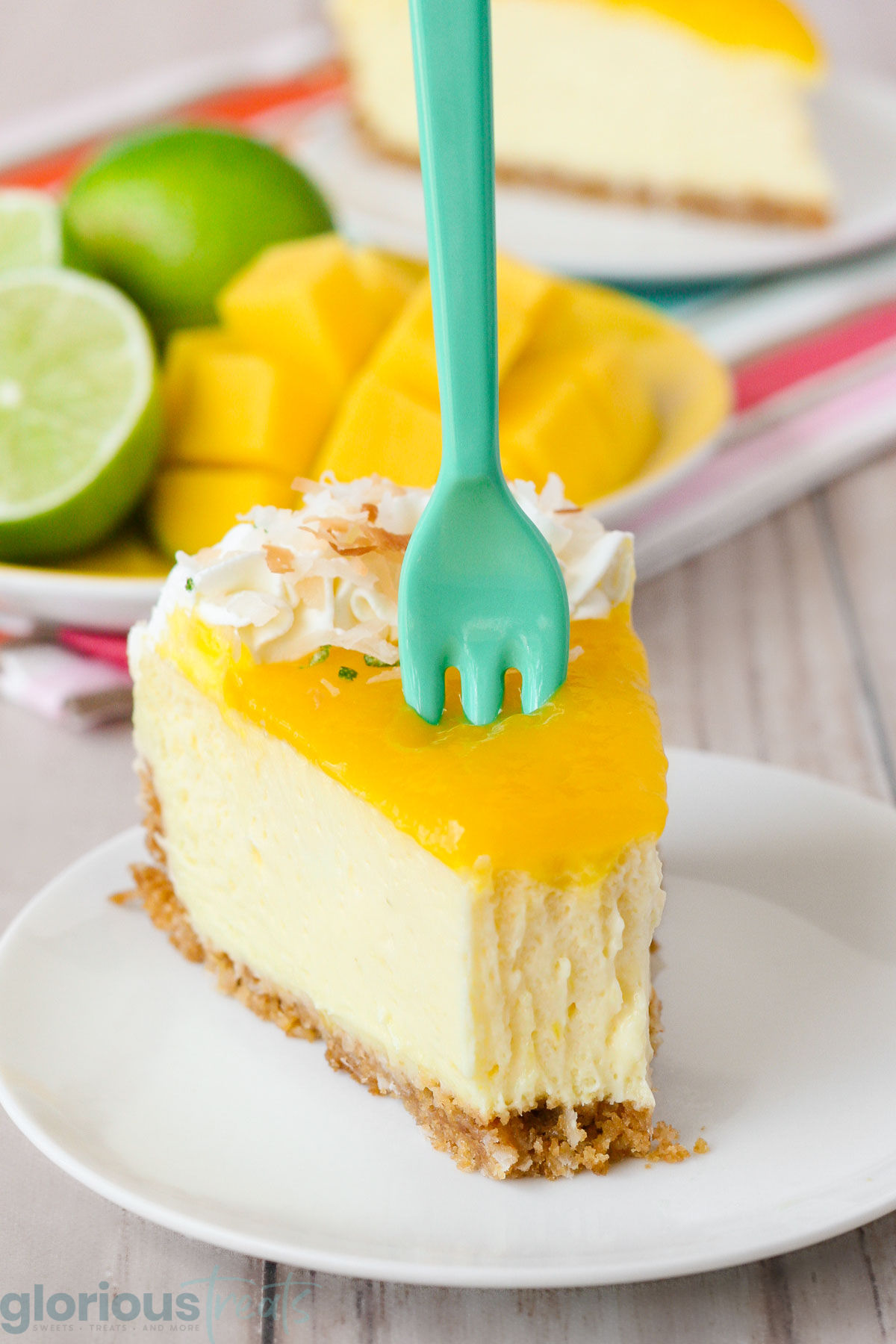 Slice of mango lime cheesecake with a forkful taken from the edge. A small plastic teal fork stuck in the cheesecake.