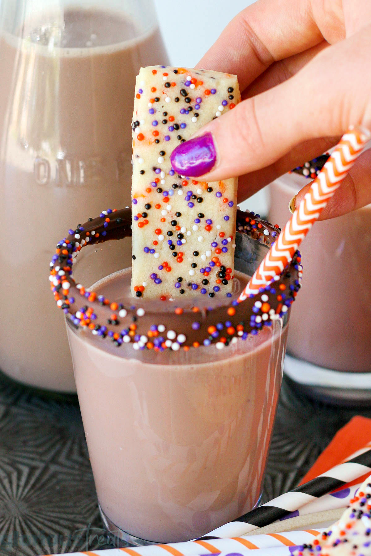 Halloween sugar cookie with sprinkles being dipped in a glass of chocolate milk.