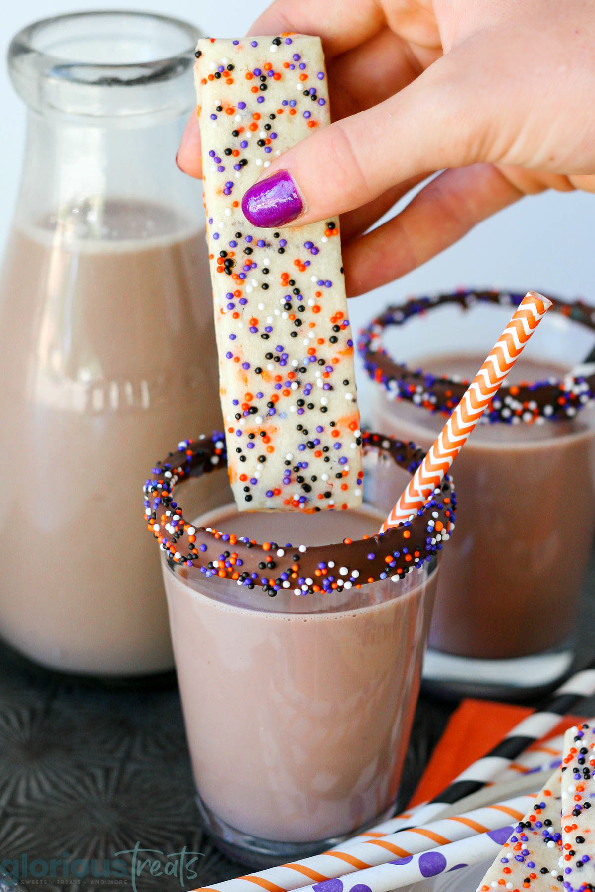 Halloween sugar cookie with sprinkles being dipped in a glass of chocolate milk.