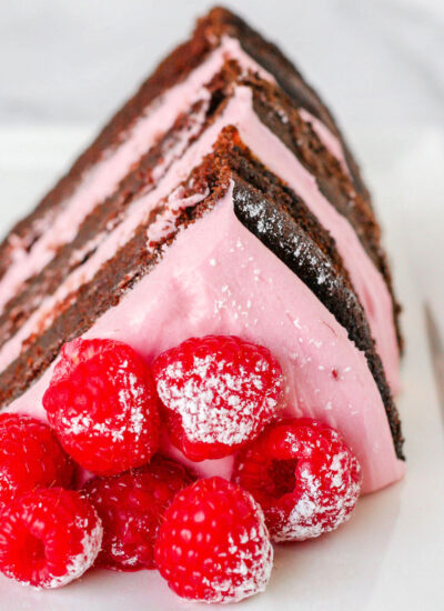 Generous slice of chocolate raspberry cake topped with fresh raspberries and sitting on a white plate.
