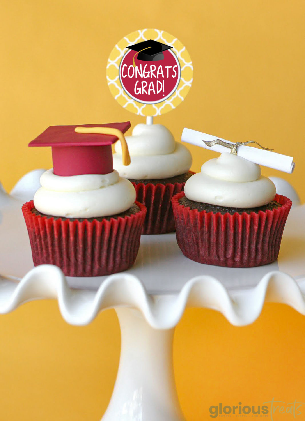 three cupcakes on a white serving platter topped with a graduation cap, a diploma, and a congrats grad decoration