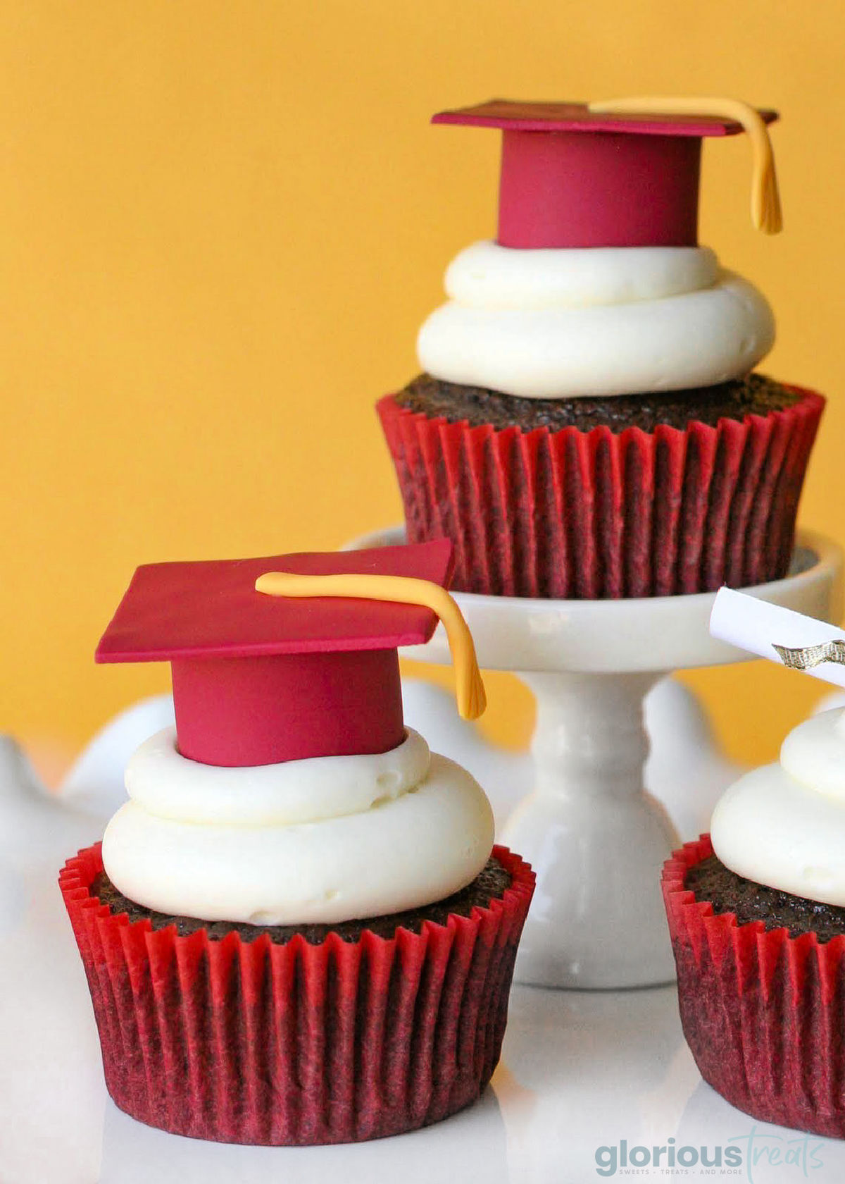 Close up of three cupcakes topped with graduation caps and tassels made with fondant. Cupcakes are in red liners.