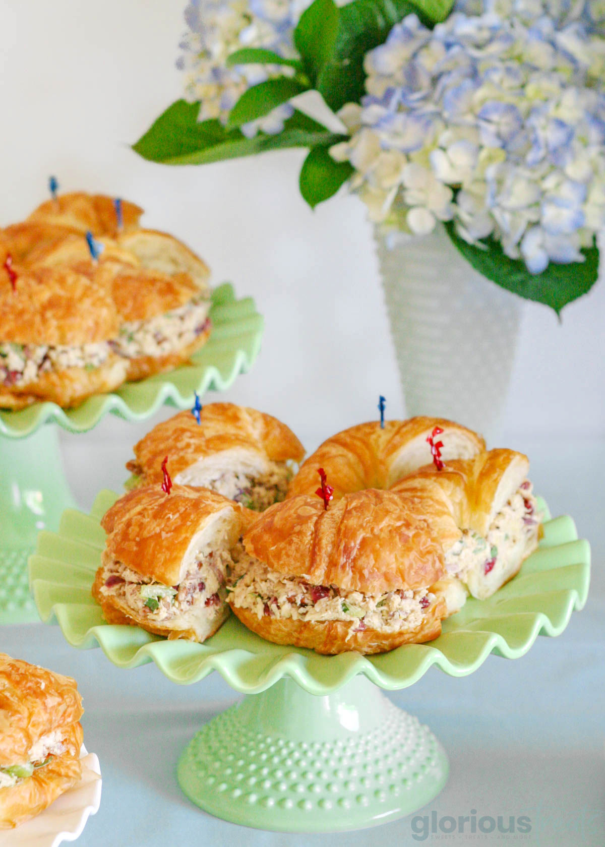 chicken salad on a croissant roll cut into smaller sandwiches and then served on a green platter