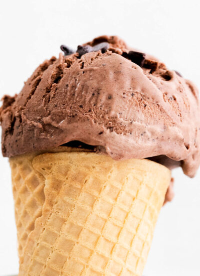 A side view of a scoop of chocolate ice cream on a cone in a glass jar.