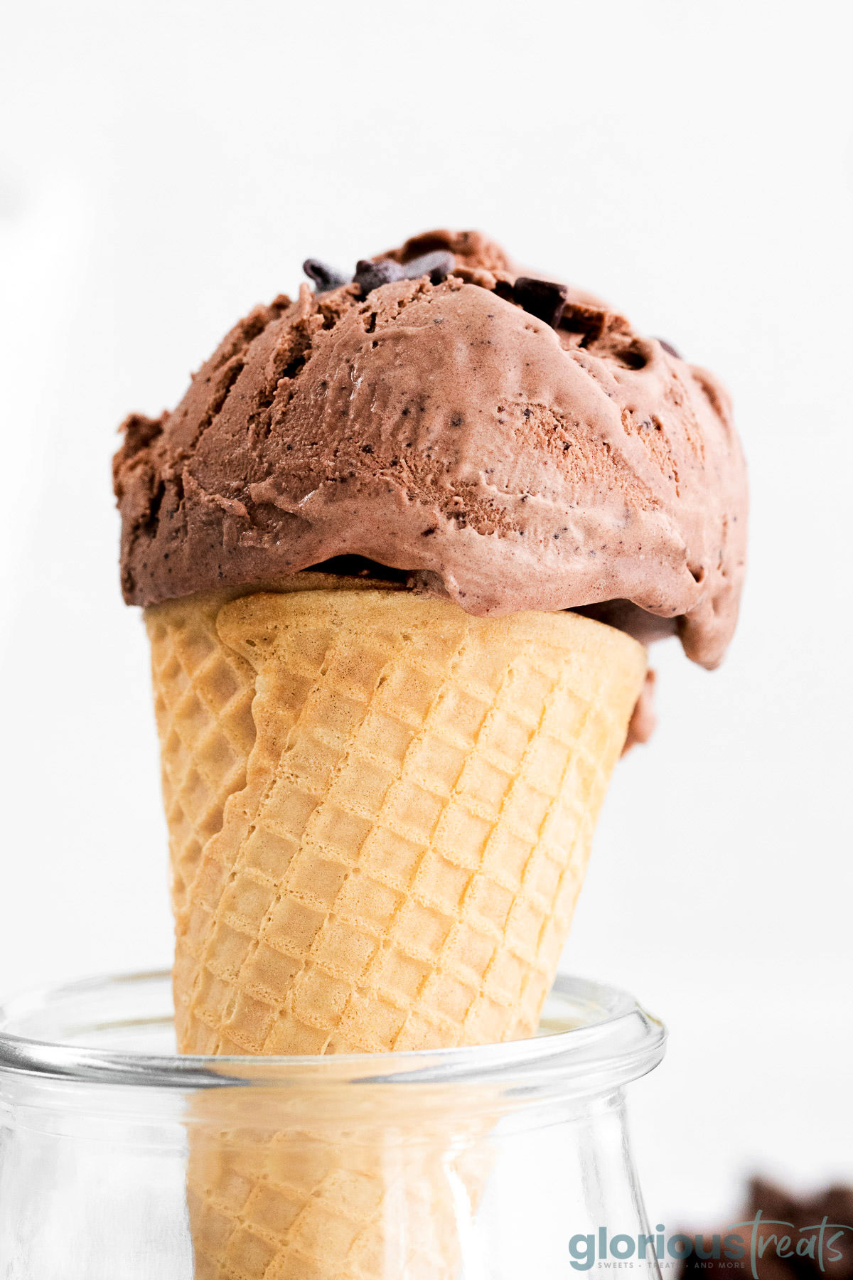 A side view of a scoop of chocolate ice cream on a cone in a glass jar.