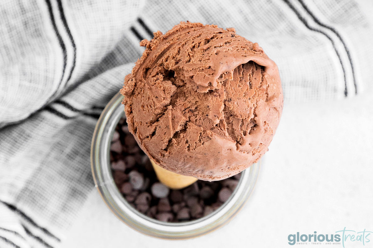 A top down shot of a scoop of no-churn chocolate ice cream on a cone in a glass jar full of chocolate chips.