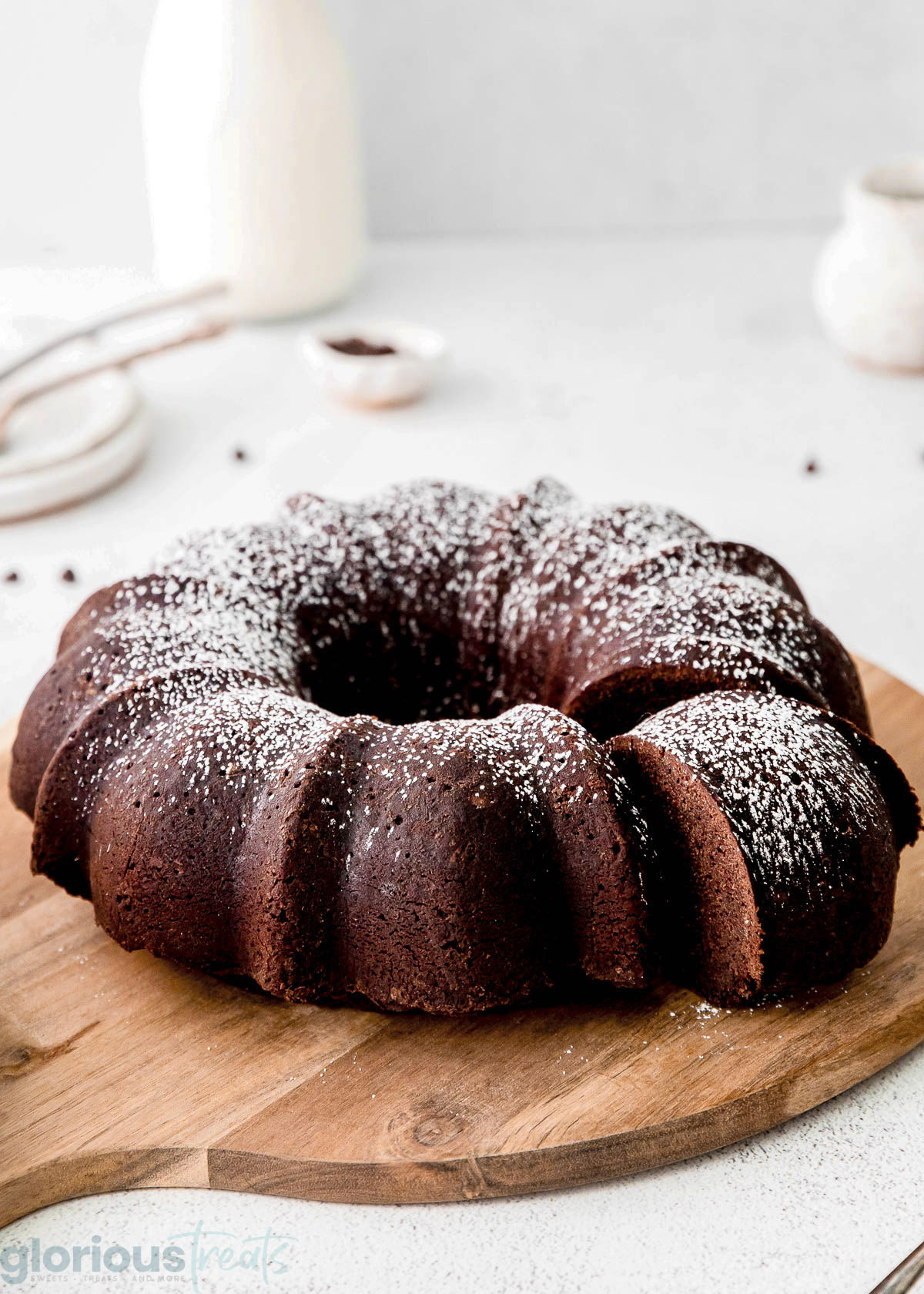 a chocolate bundt cake on a wood cutting board with a slice taken out of it.