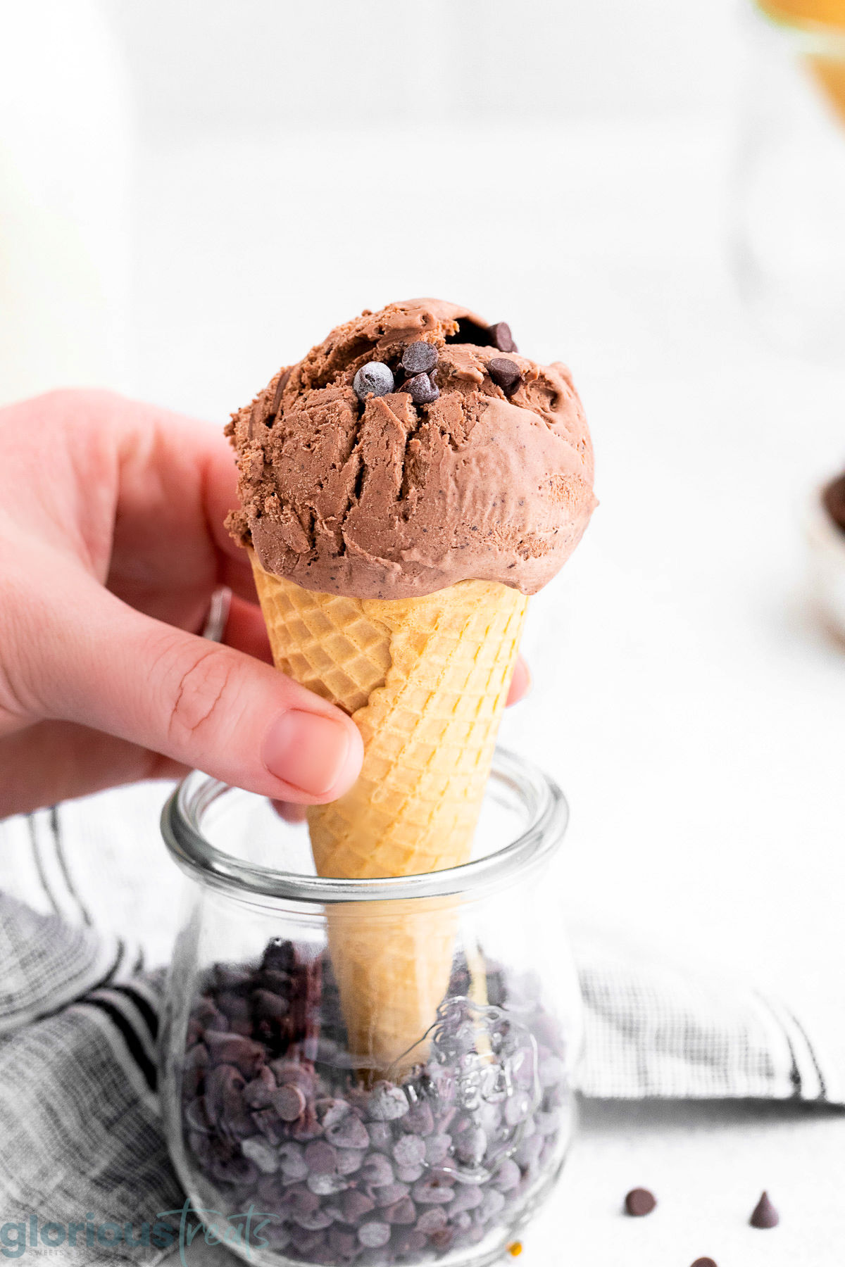 A side view of a hand grabbing the ice cream cone with a scoop of no-churn chocolate ice cream on top.