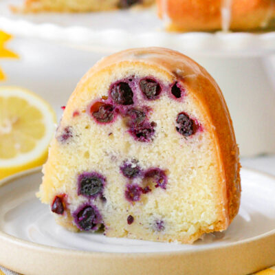 a slice of lemon blueberry bundt cake on a white plate with visible chunks of blueberry in it