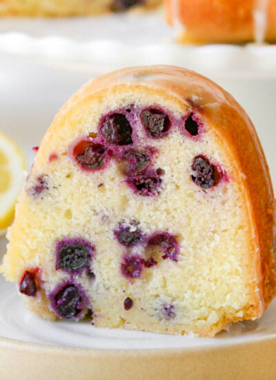 a slice of lemon blueberry bundt cake on a white plate with visible chunks of blueberry in it