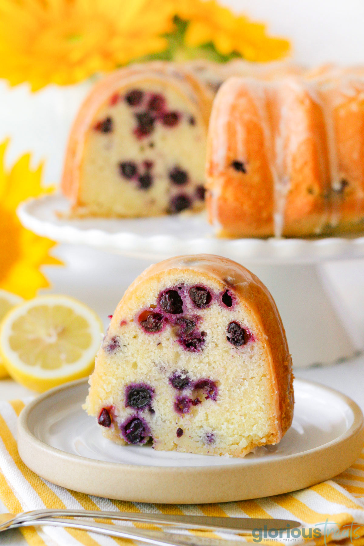 a slice of blueberry lemon bundt cake on a white plate with the full cake in the background