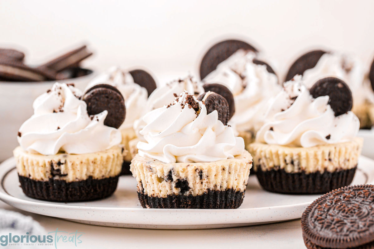 Small white plate with four mini oreo cheesecakes on the plate topped with whipped cream and mini oreos.