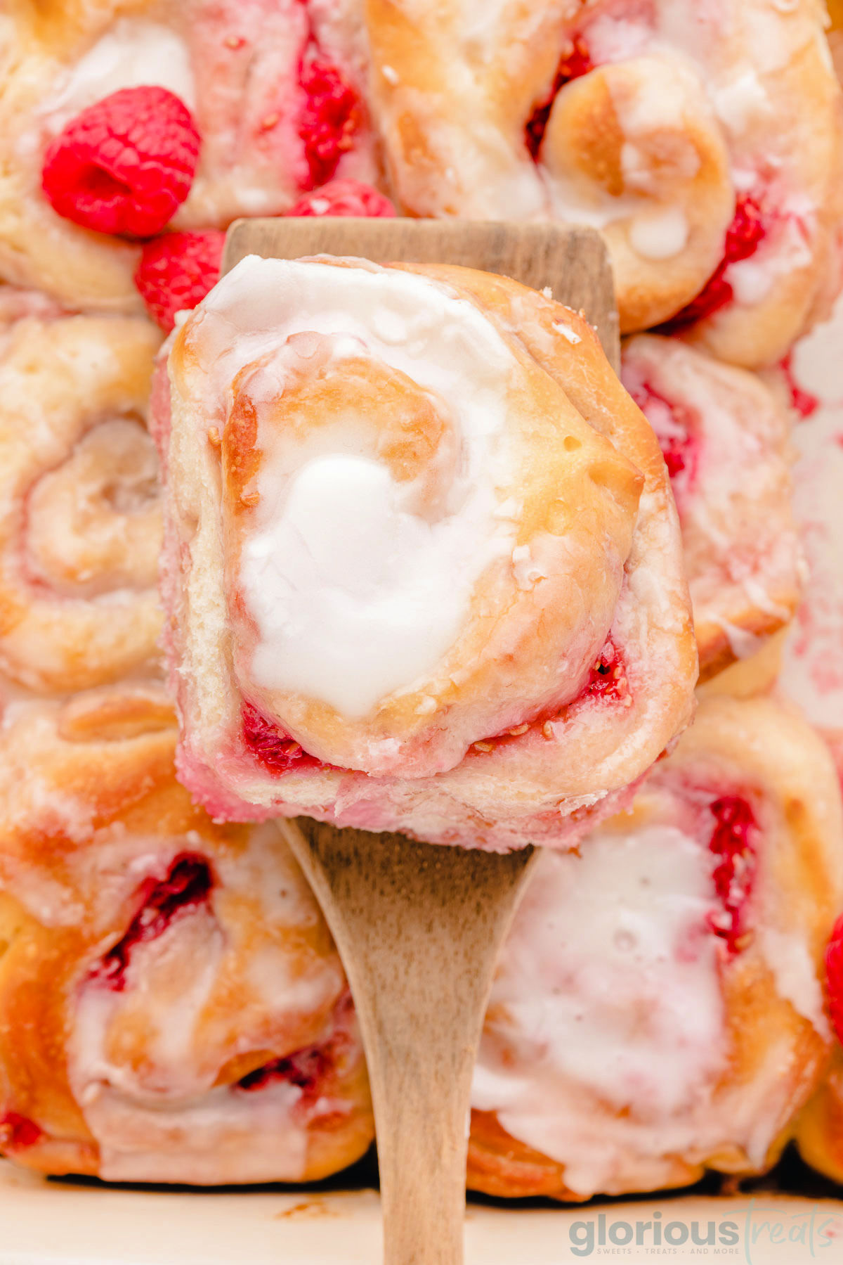 a top down view of a raspberry sweet roll being lifted above a pan filled with rolls.