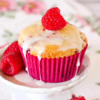 a raspberry lemon muffin topped with icing and a fresh raspberry on a white plate