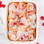 a top down shot of a pan of raspberry sweet rolls on a white surface.