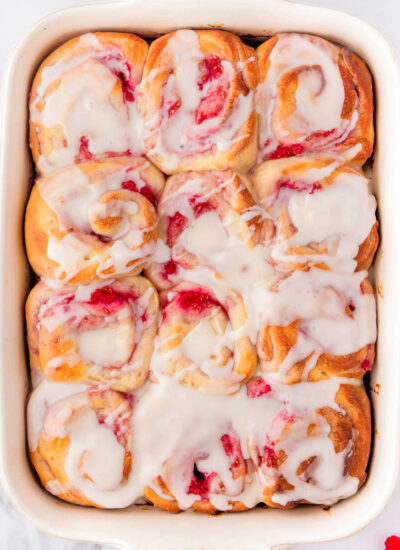 a top down shot of a pan of raspberry sweet rolls on a white surface.