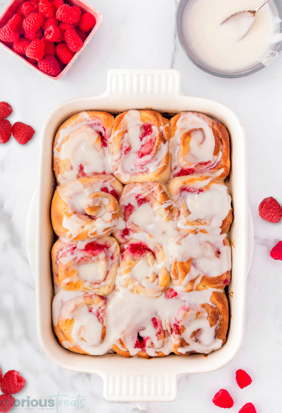 a top down shot of a pan of raspberry sweet rolls on a white surface.