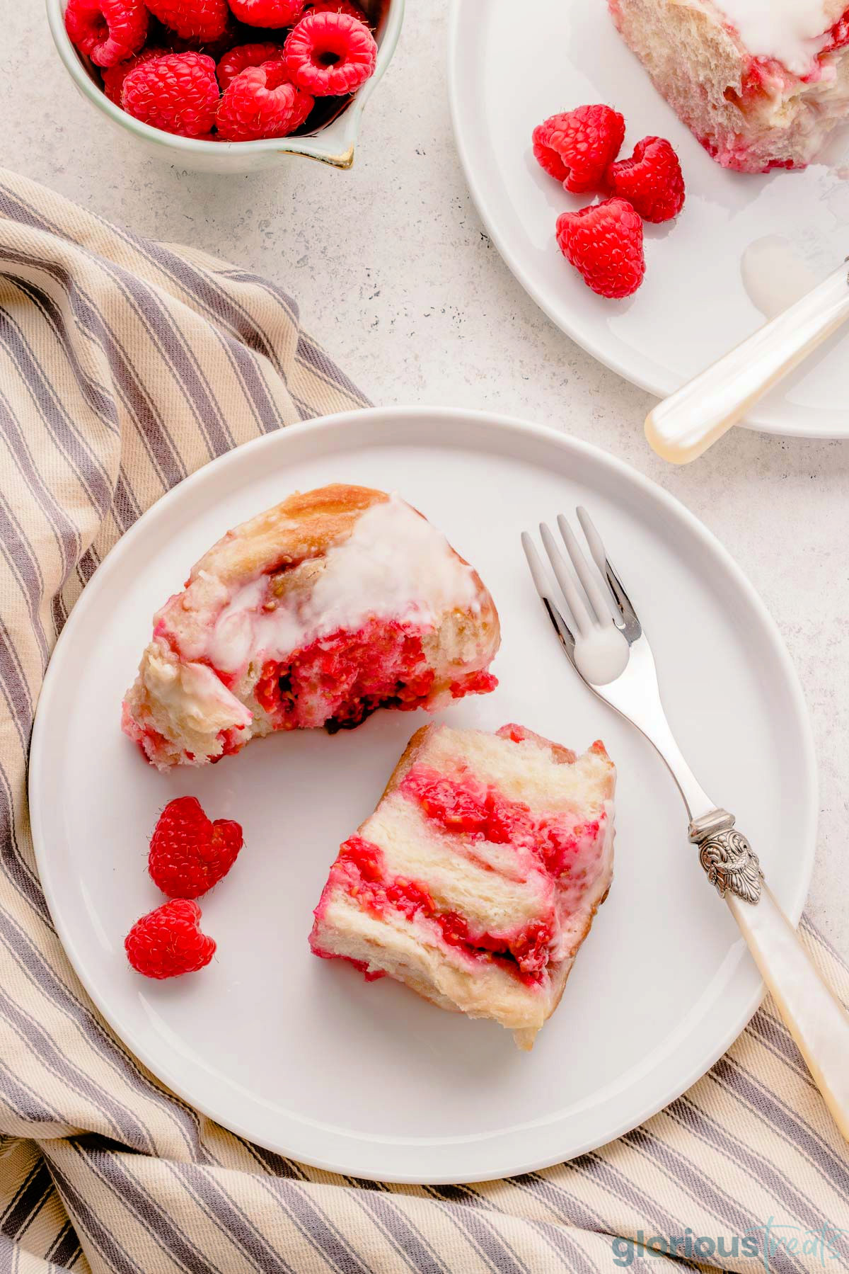 a raspberry sweet roll cut in half and placed on a white plate with raspberries.