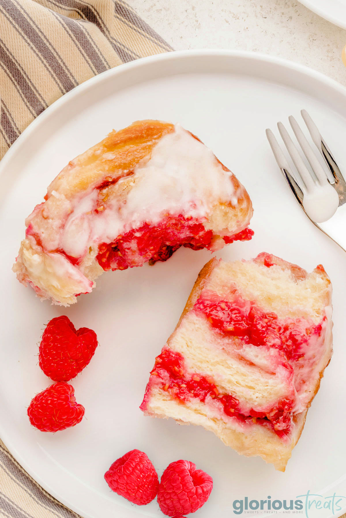 a raspberry sweet roll cut in half and placed on a white plate with raspberries.