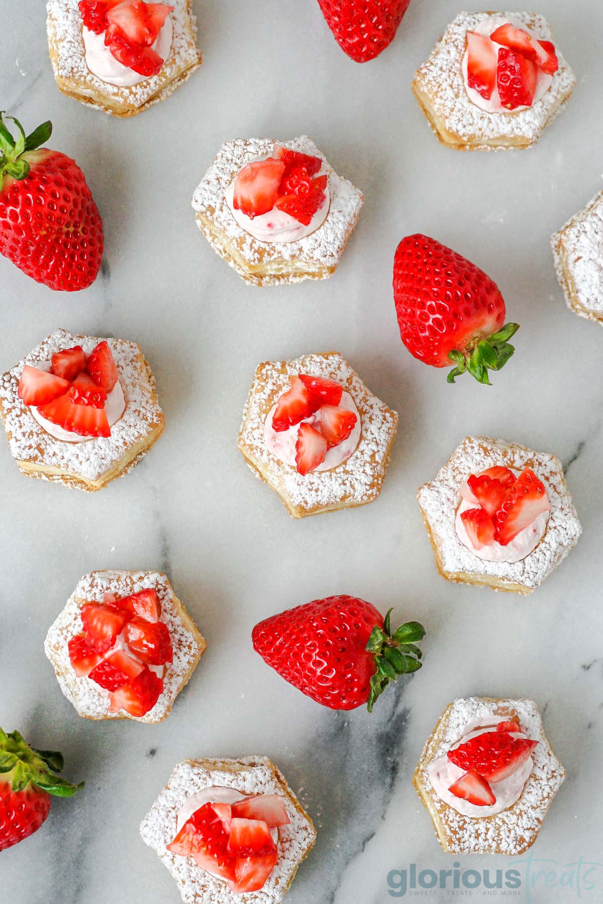 overhead view of strawberry cream puffs topped with chopped strawberries and dusted with powdered sugar, with some whole strawberries pictured between the pastries