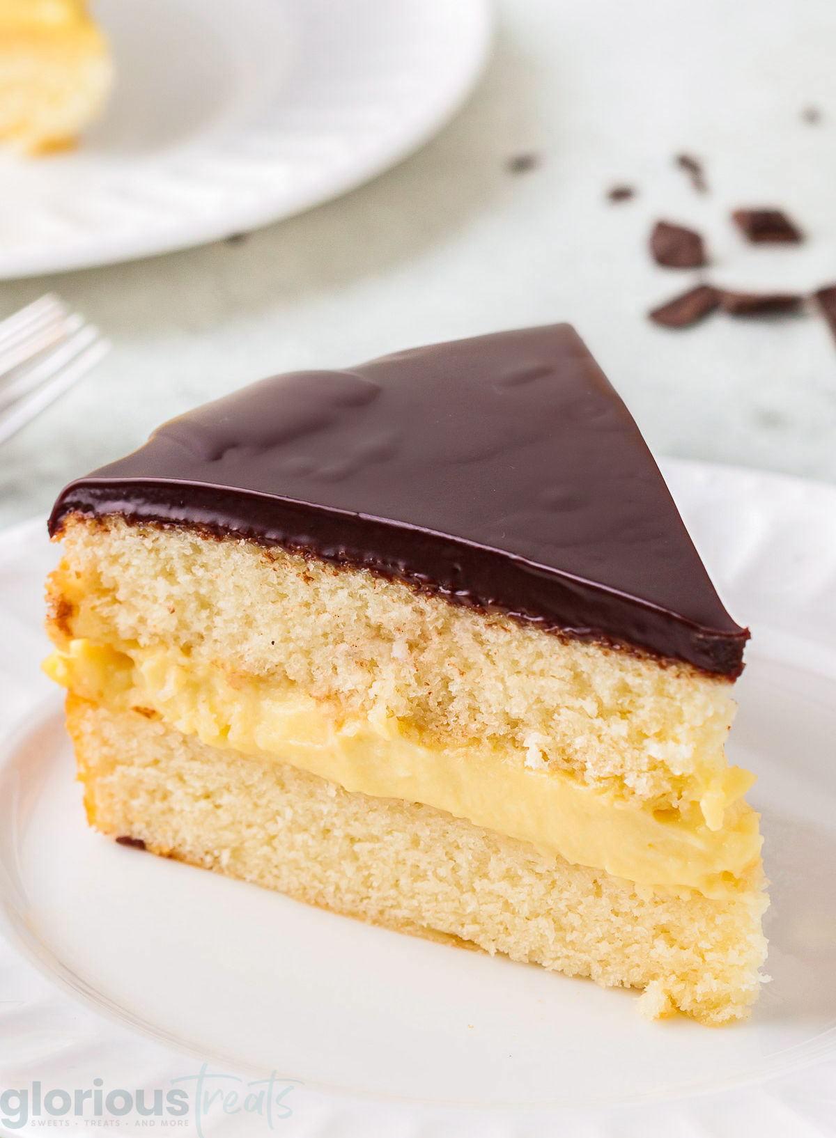 A slice of boston cream pie on a white plate.