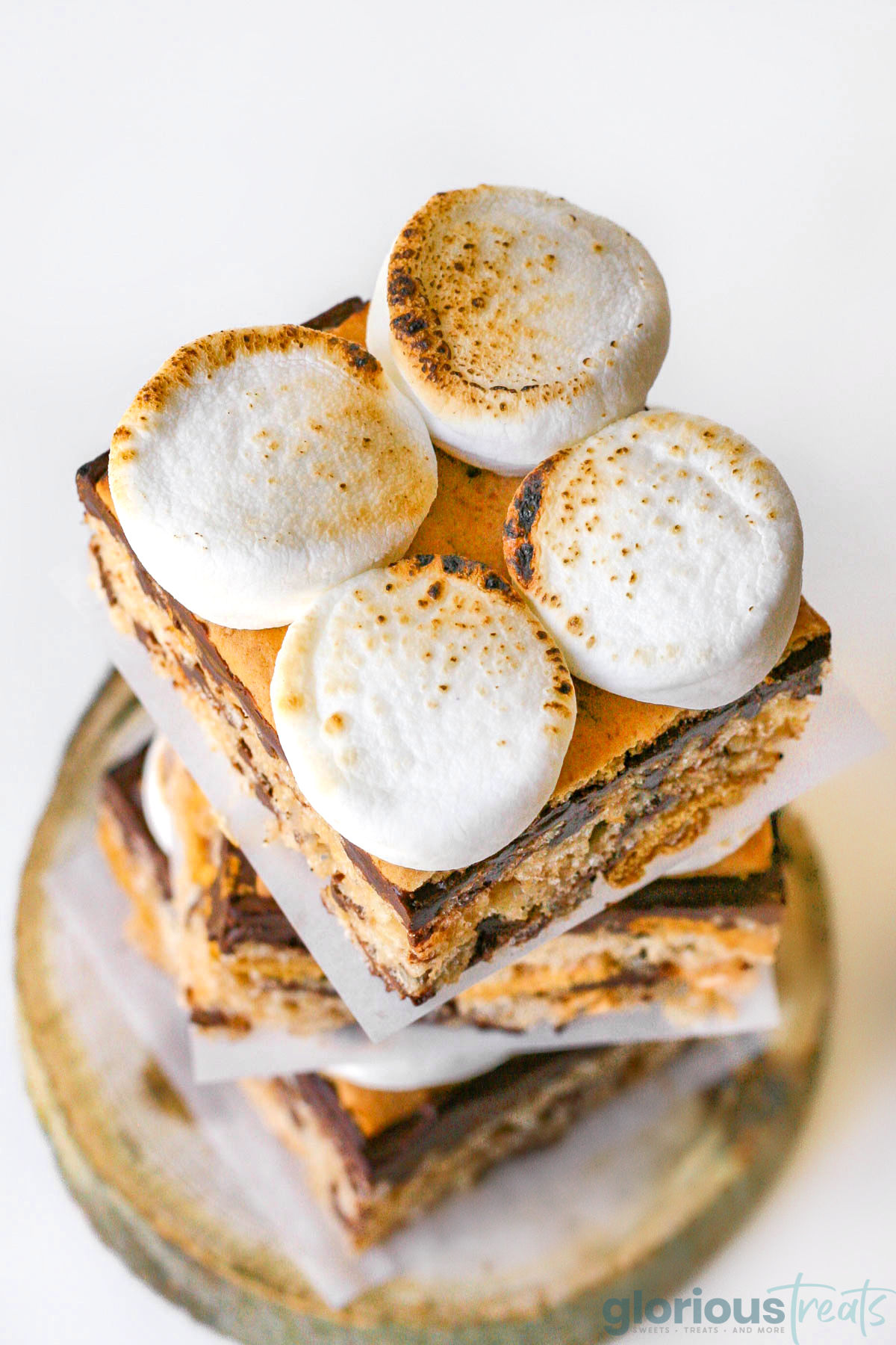 Top down view of smores rice krispie treats stacked on a small log. You can see 4 toasted marshmallows on top of the treat.