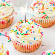 Birthday cupcakes on a white surface with a candle in one of them.