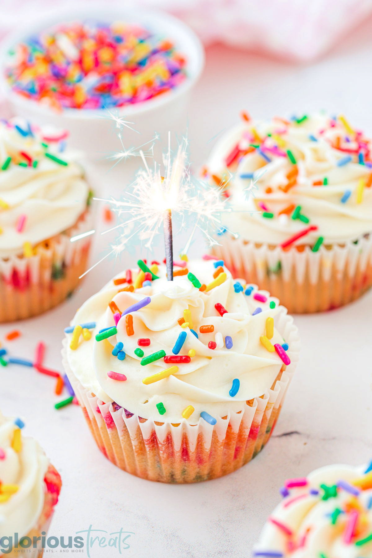 Birthday cupcakes on a white surface with a lit candle on one of them.