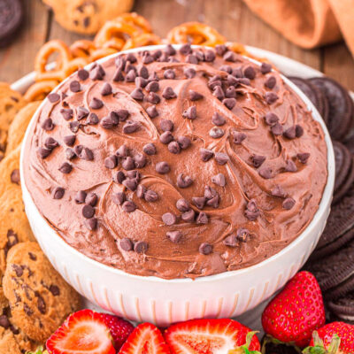 A close up shot of brownie batter dip in a white bowl next to an assortment of dippers.