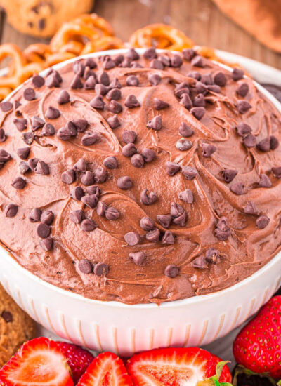 A close up shot of brownie batter dip in a white bowl next to an assortment of dippers.