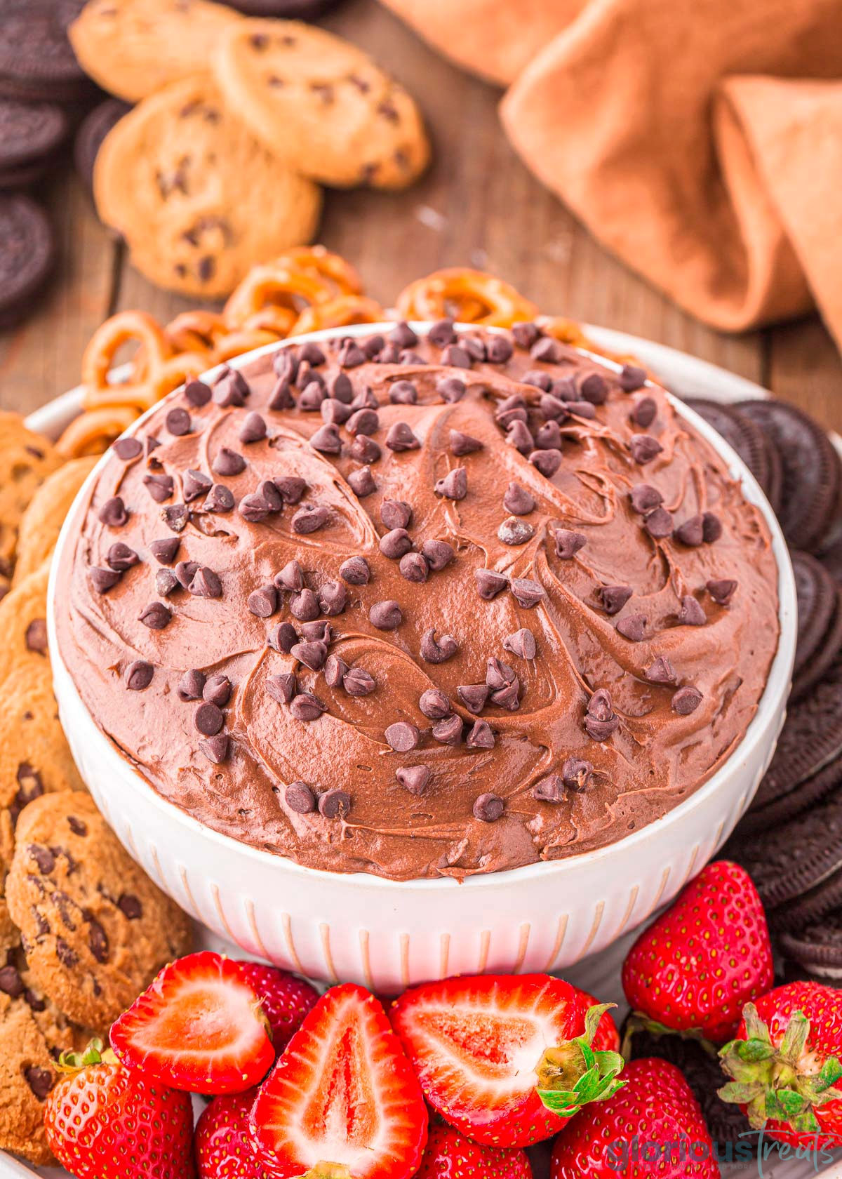 A close up shot of brownie batter dip in a white bowl next to an assortment of dippers.