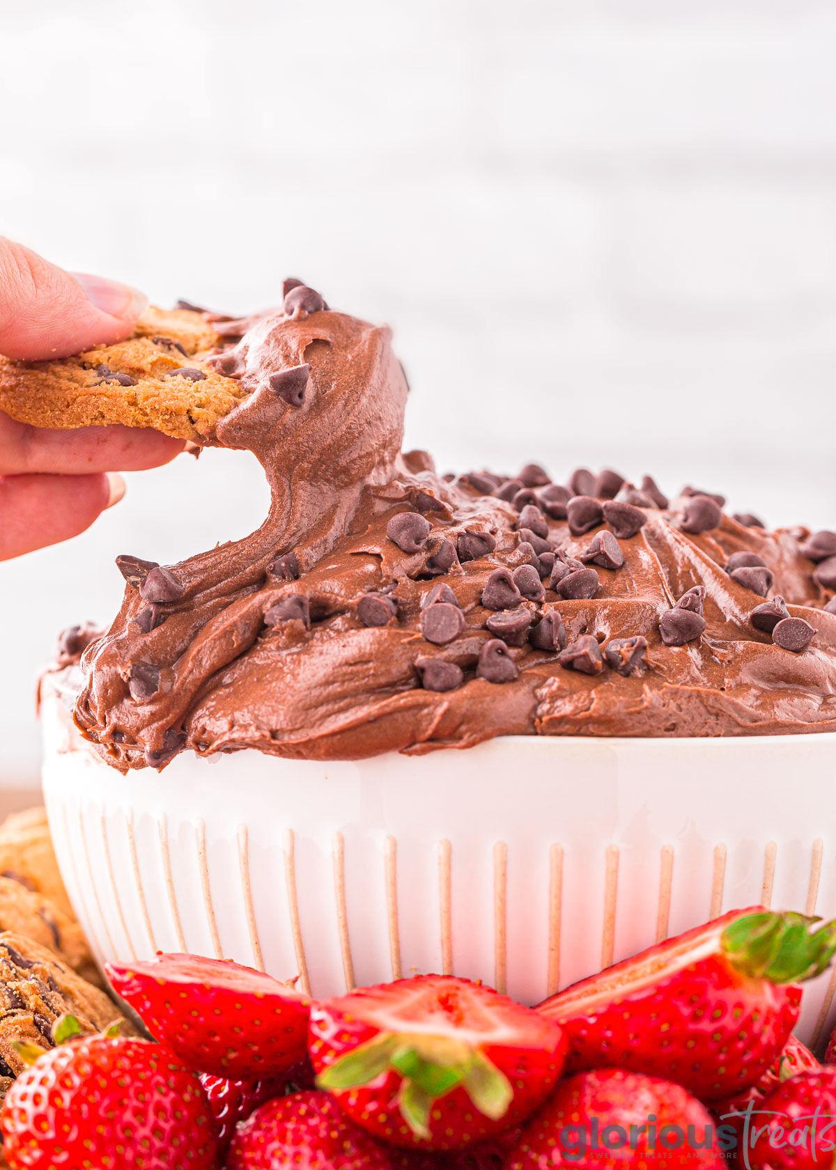 A hand dipping a cookie into brownie batter dip in a white bowl.