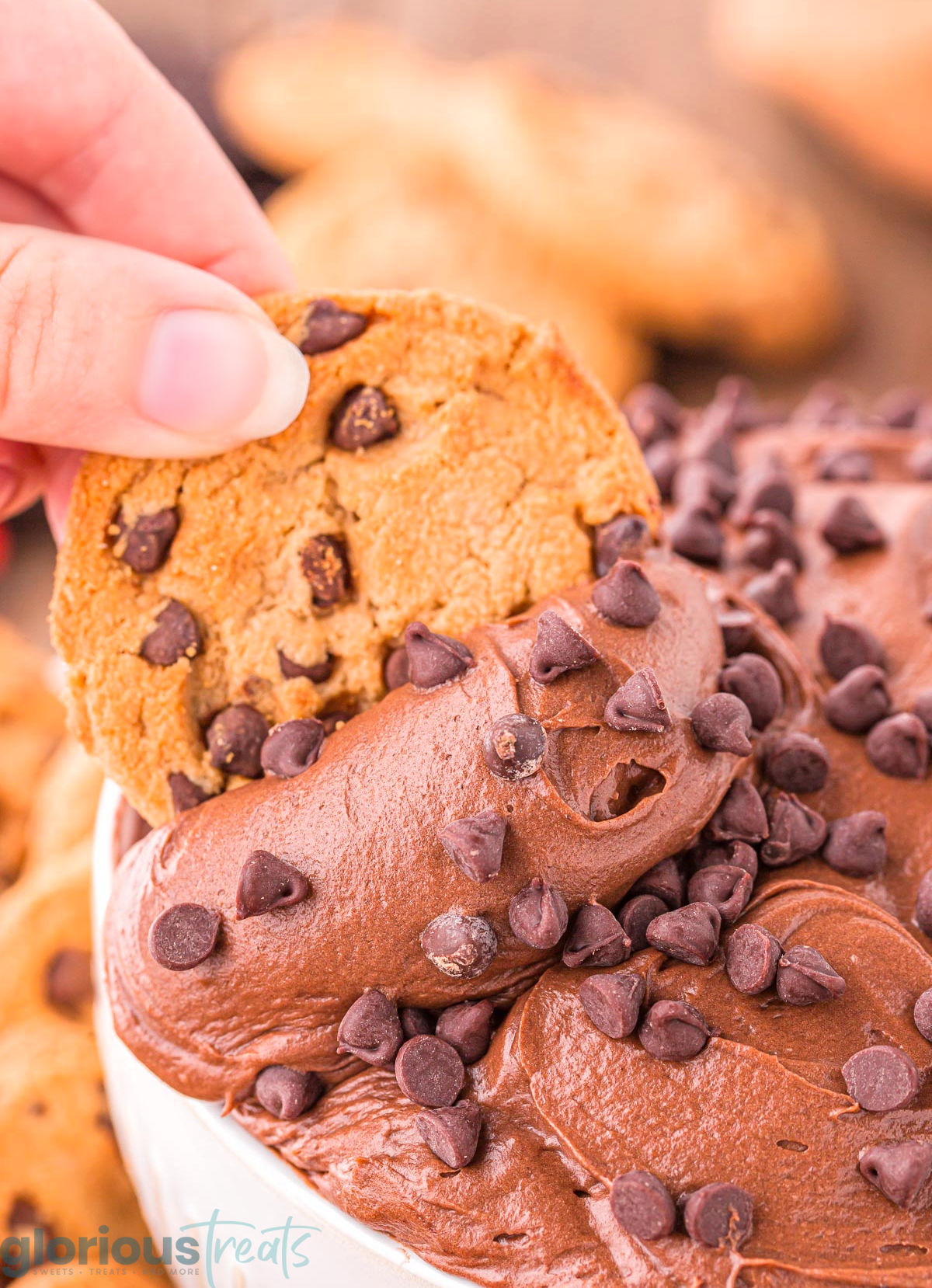 A close up shot of a hand dipping a cookie in brownie batter dip.