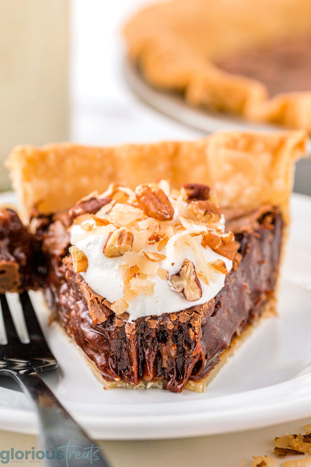 A slice of german chocolate pie with a bite taken out of it on a white plate.