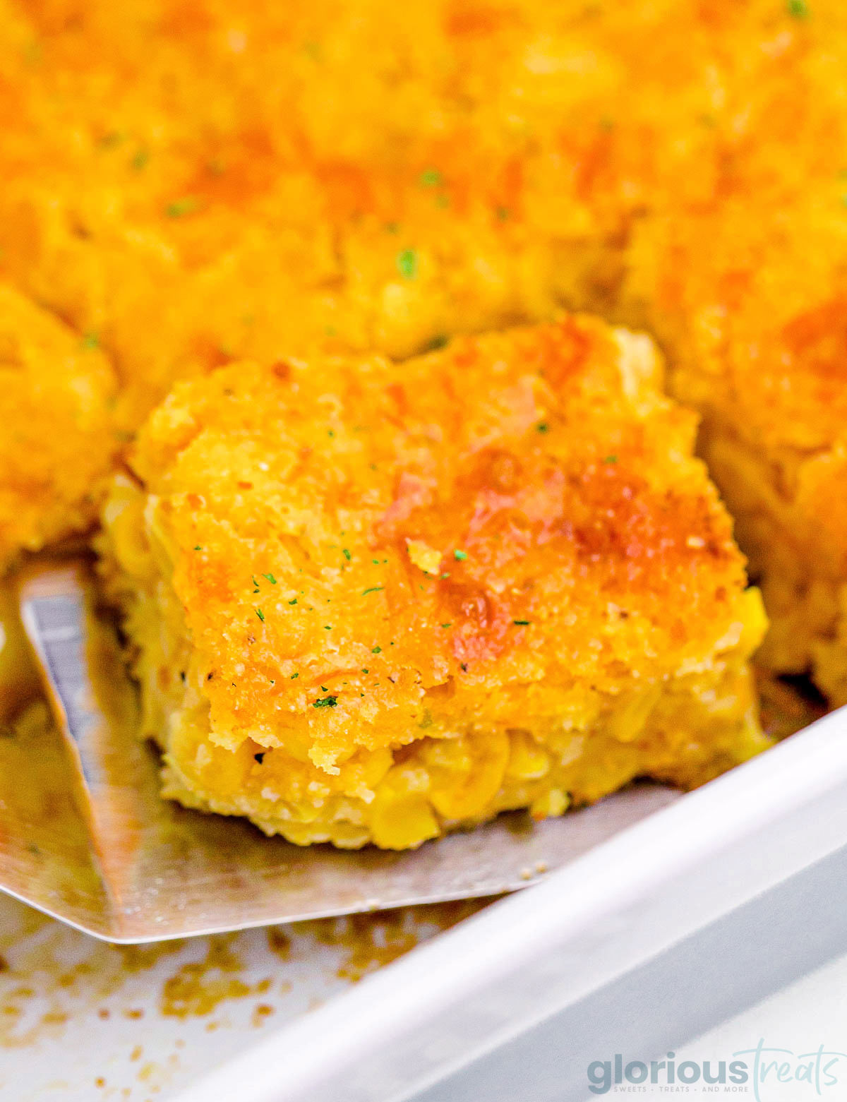 A spatula holding a piece of cornbread casserole in a white pan.