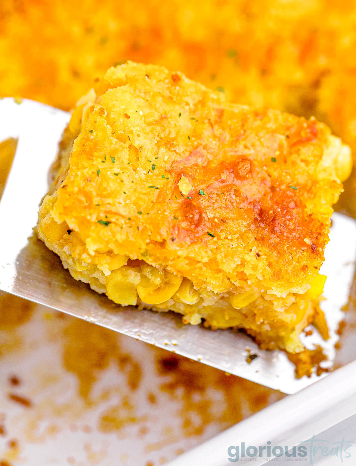 A spatula holding a piece of cornbread casserole in a white pan.