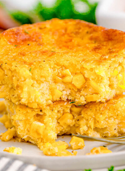 A fork digging into a piece of cornbread casserole on a white plate.