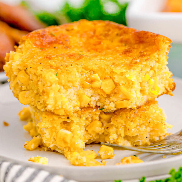 A fork digging into a piece of cornbread casserole on a white plate.