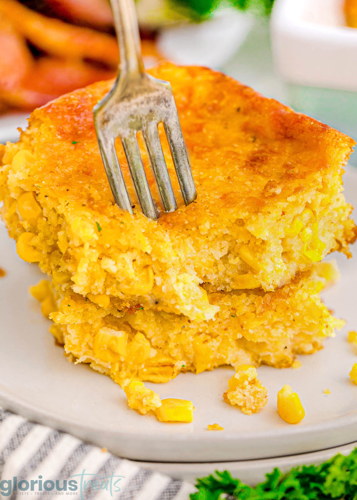 A fork digging into a piece of cornbread casserole on a white plate.