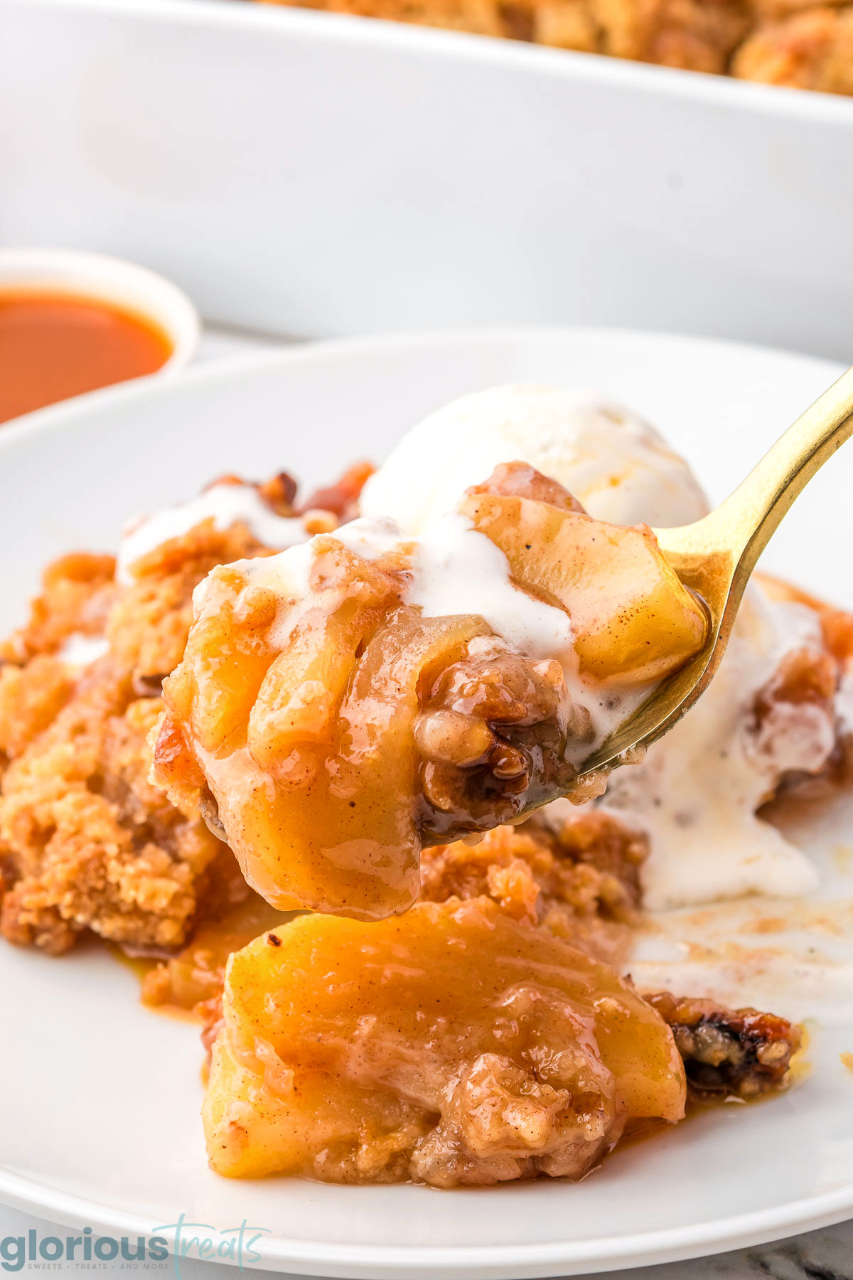 A fork holding up a biteful of apple crumble over a white plate with a serving of crumble on it.