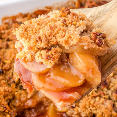 Close up view of a wood spatula holding up a serving of apple crumble.