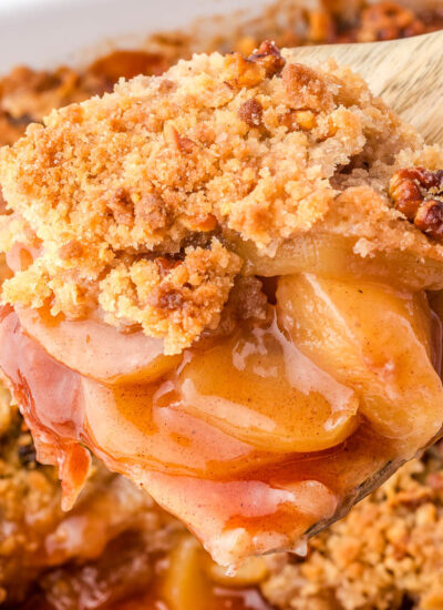 Close up view of a wood spatula holding up a serving of apple crumble.