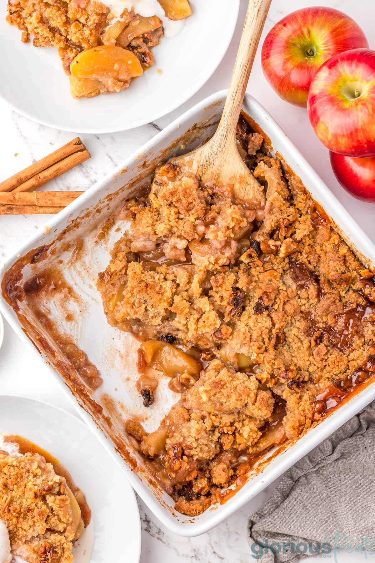 A wood spatula in the corner of a white pan with apple crumble.