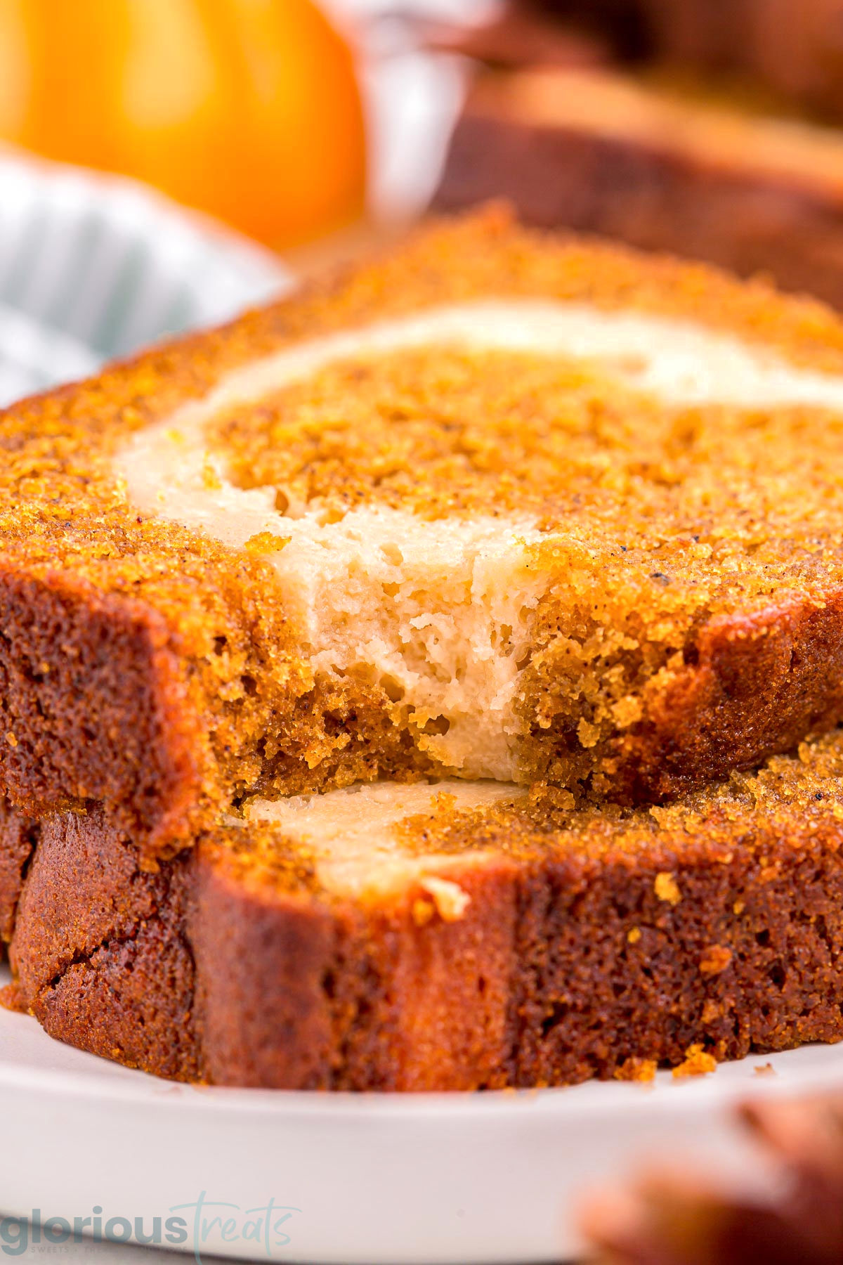 Two slices of pumpkin cheese bread stacked on a white plate. The top slice has a bite taken out of it.