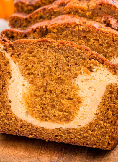 A close up view of a loaf of pumpkin cream cheese bread. The loaf is cut into slices.