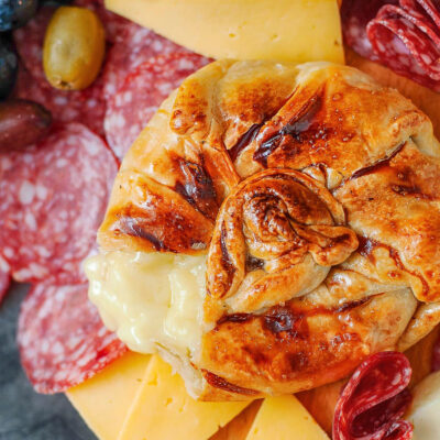 Honey baked brie wrapped in puff pastry. Salami and cheese are on the platter with the brie.