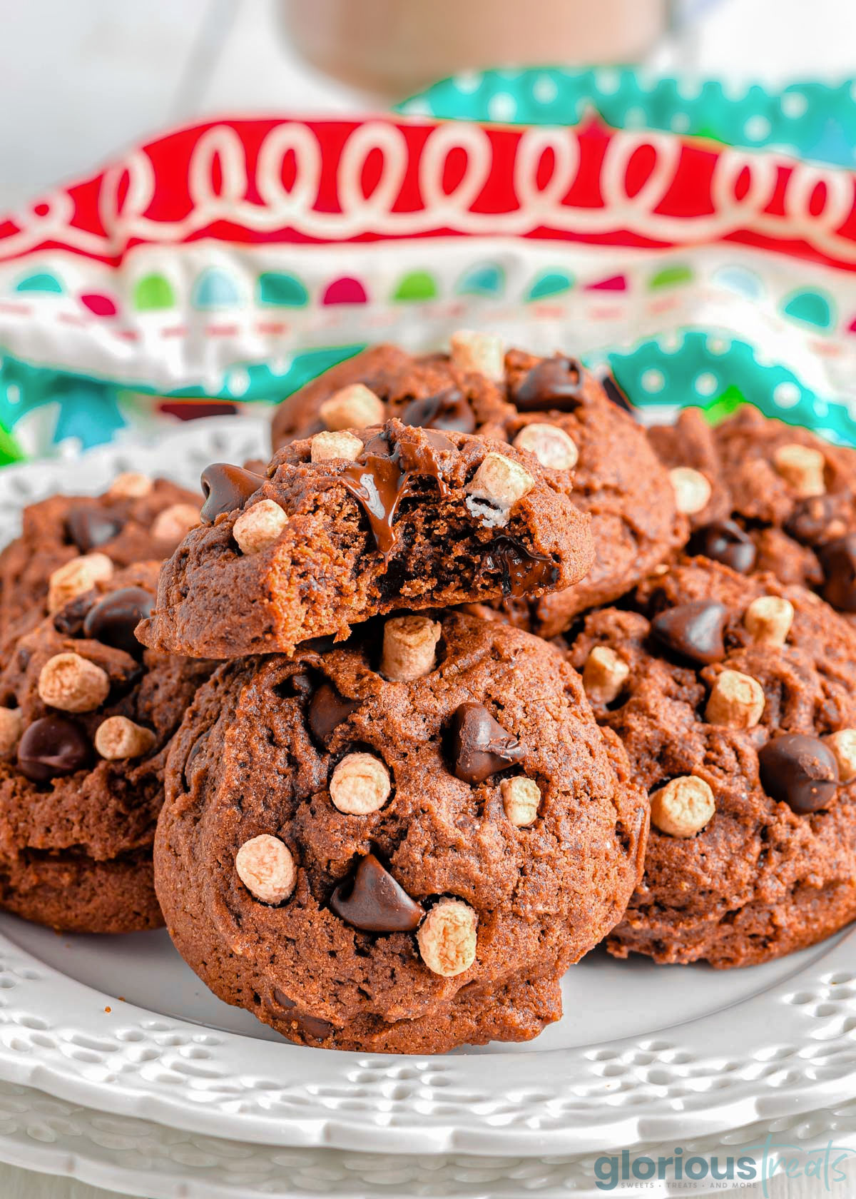 Hot Chocolate Cookies on a white plate with a festive linen in the background. One of the cookies has a bite taken out of it.