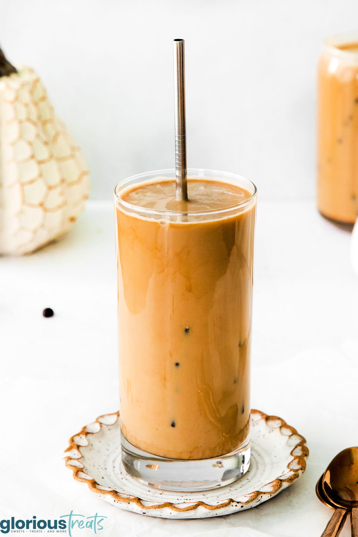 A glass of pumpkin cream cold brew with a metal straw sticking out of it. The glass is on a decorative plate.